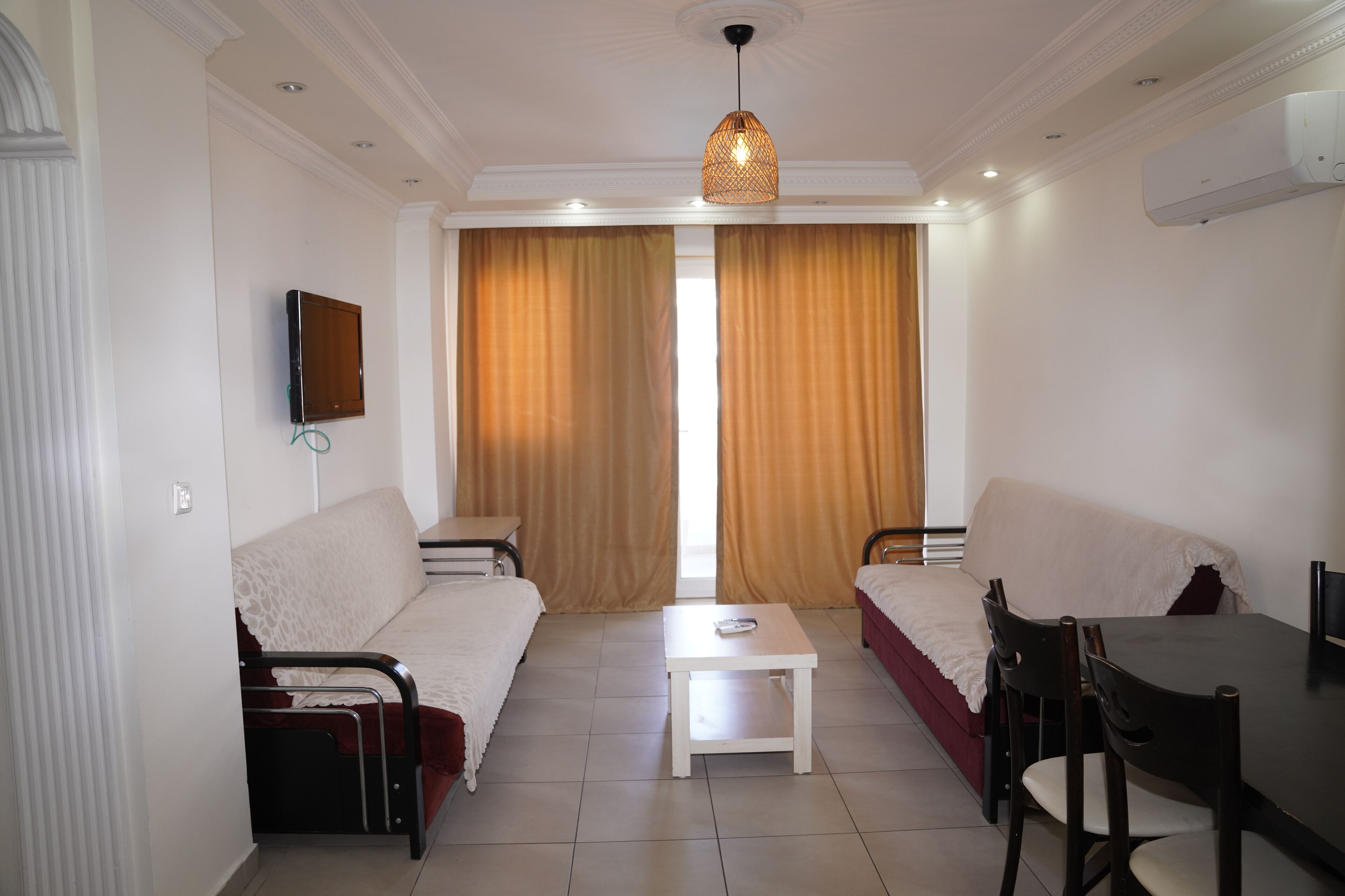 A room with a bed, a sofa, a dining table with chairs, a small white table, and a hanging light fixture.