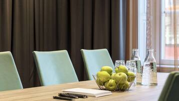 Una mesa de conferencias con un bol de manzanas verdes, un cuaderno, bolígrafos y dos botellas de vidrio sobre una mesa de madera.