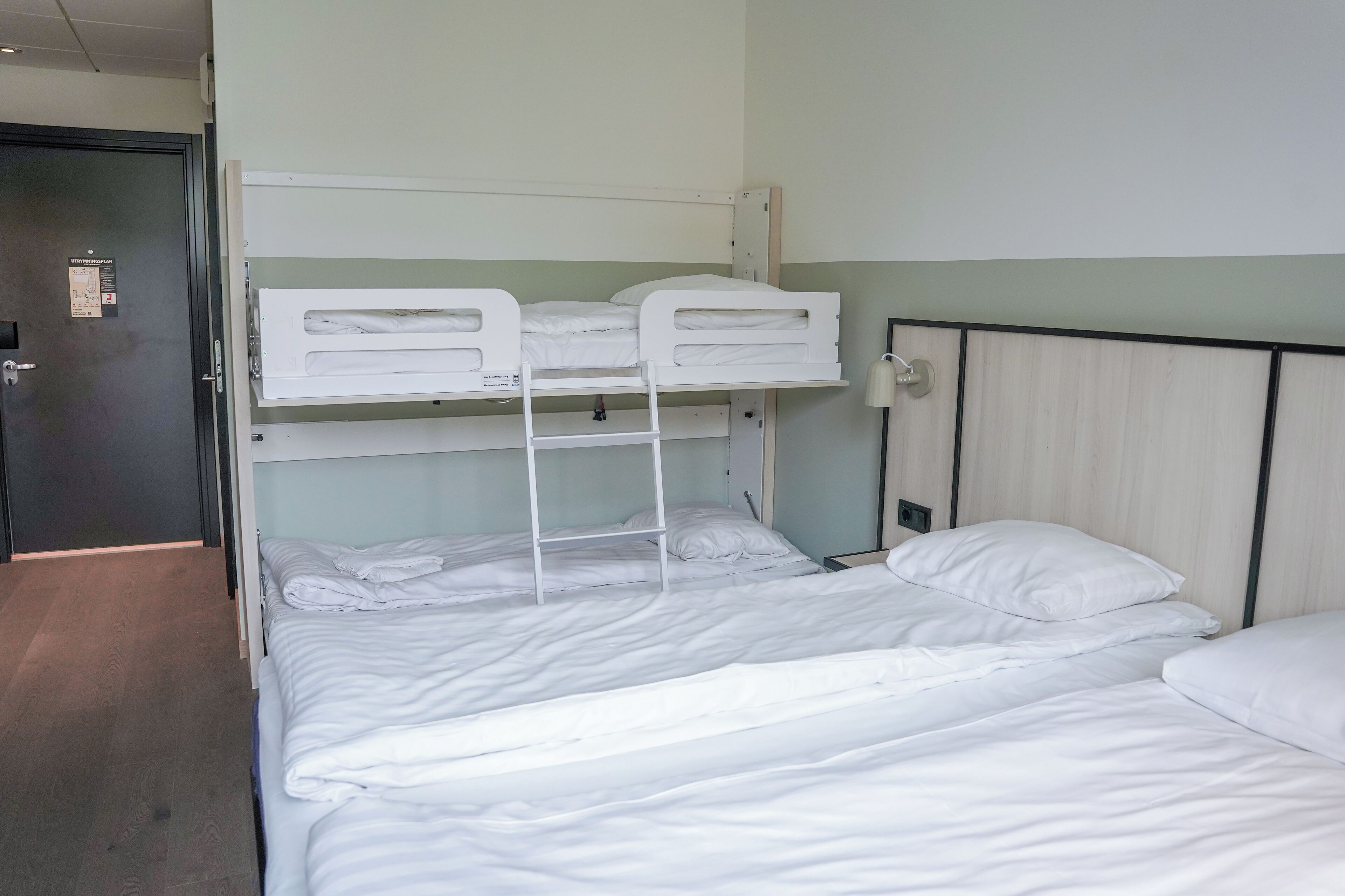 Habitación con literas, cabecero de madera, mesita de noche y lámpara de pared.