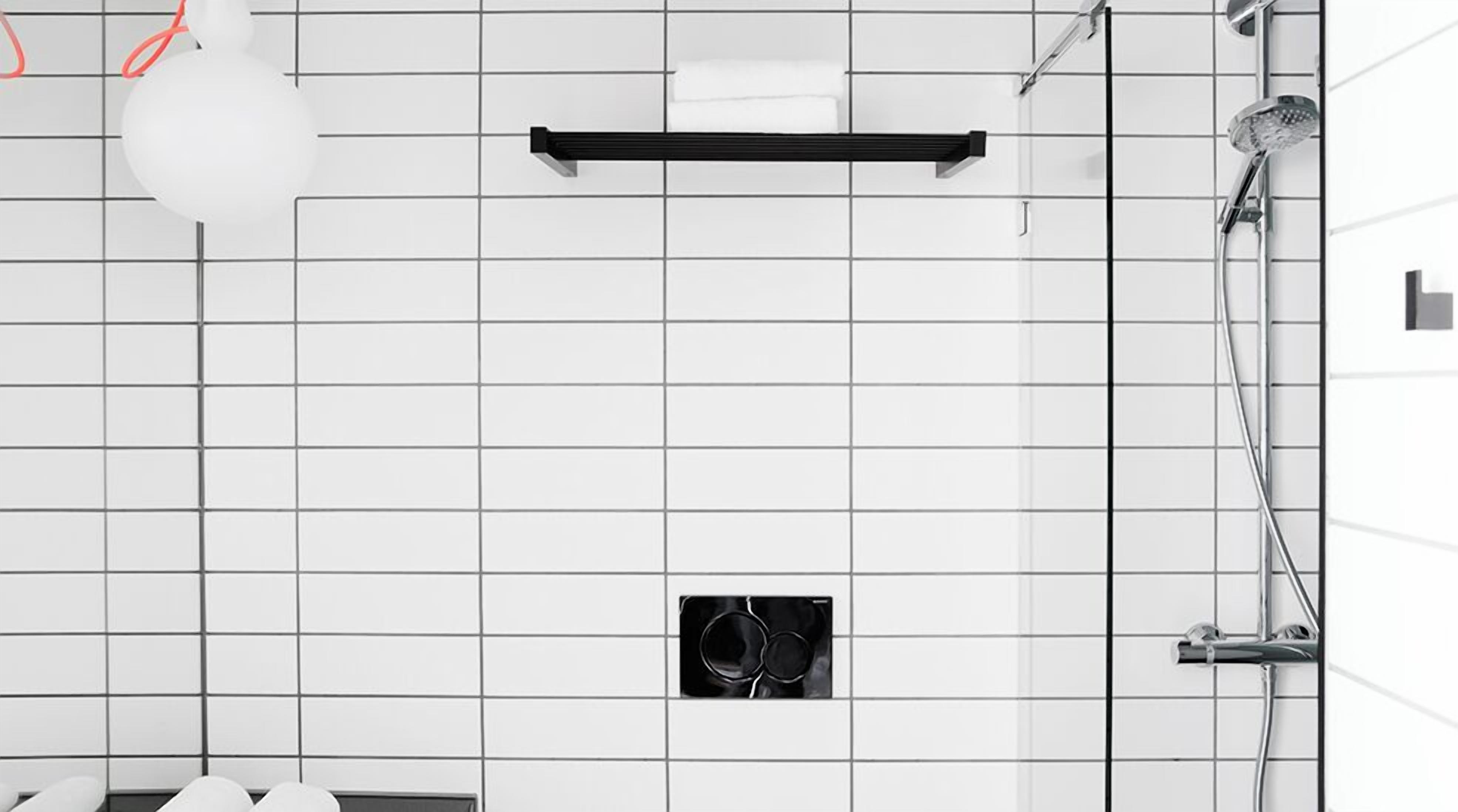 Un baño con azulejos blancos, un perchero negro, un cabezal de ducha y una unidad de ventilación.