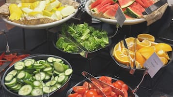 A buffet with various food items including sliced cucumbers, tomatoes, watermelon, and oranges.