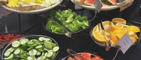 A buffet with various food items including sliced cucumbers, tomatoes, watermelon, and oranges.