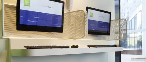 An office space with two interactive kiosks, a white desk, and teal stools.