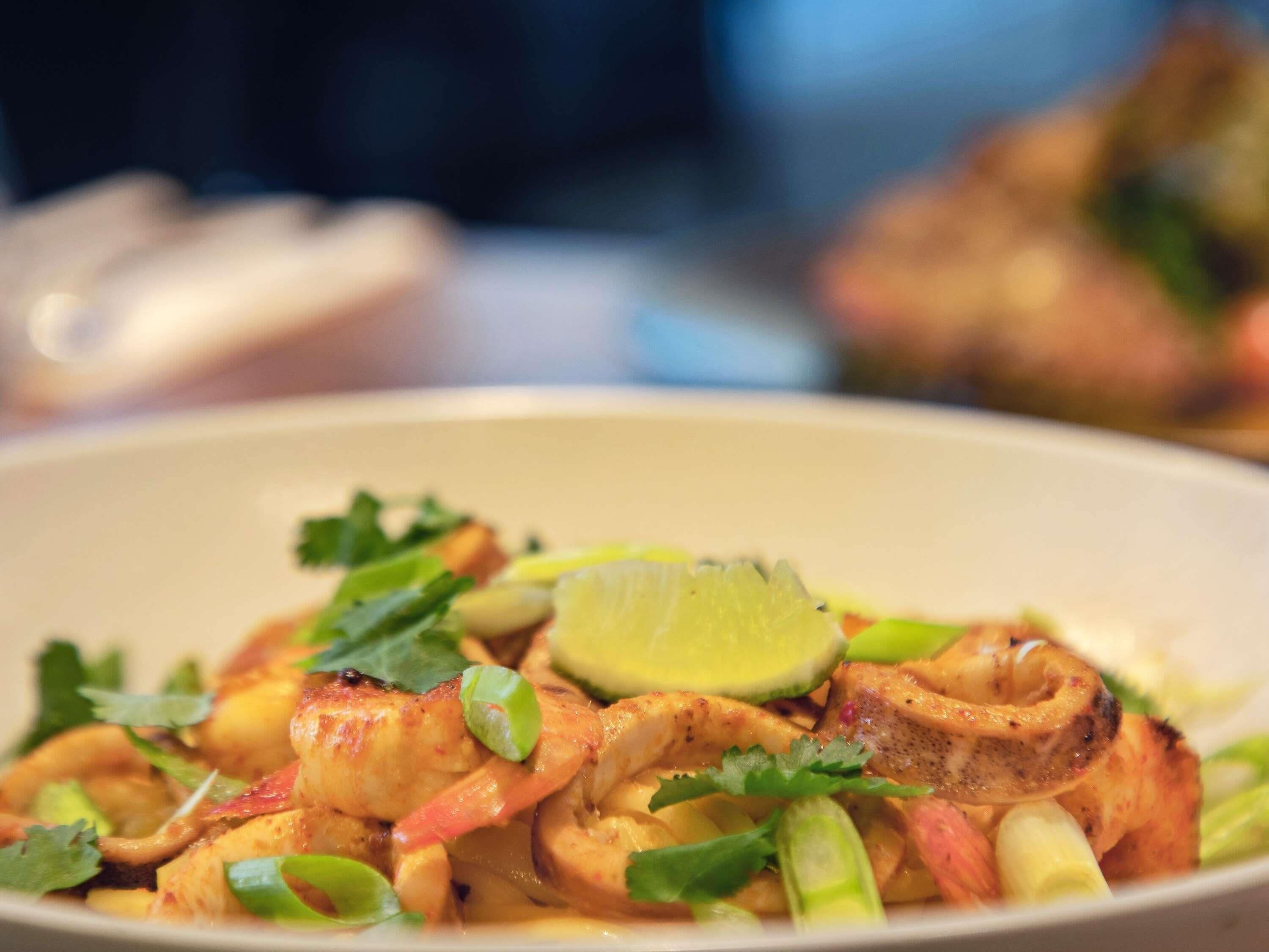 A bowl of food with shrimp, lime, and cilantro.
