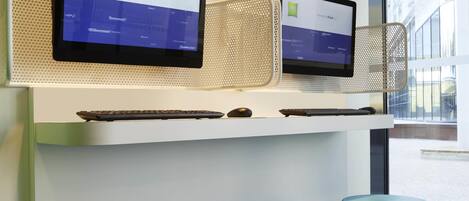 Two monitors on a white desk with a keyboard and mouse, a speaker, and teal stools.