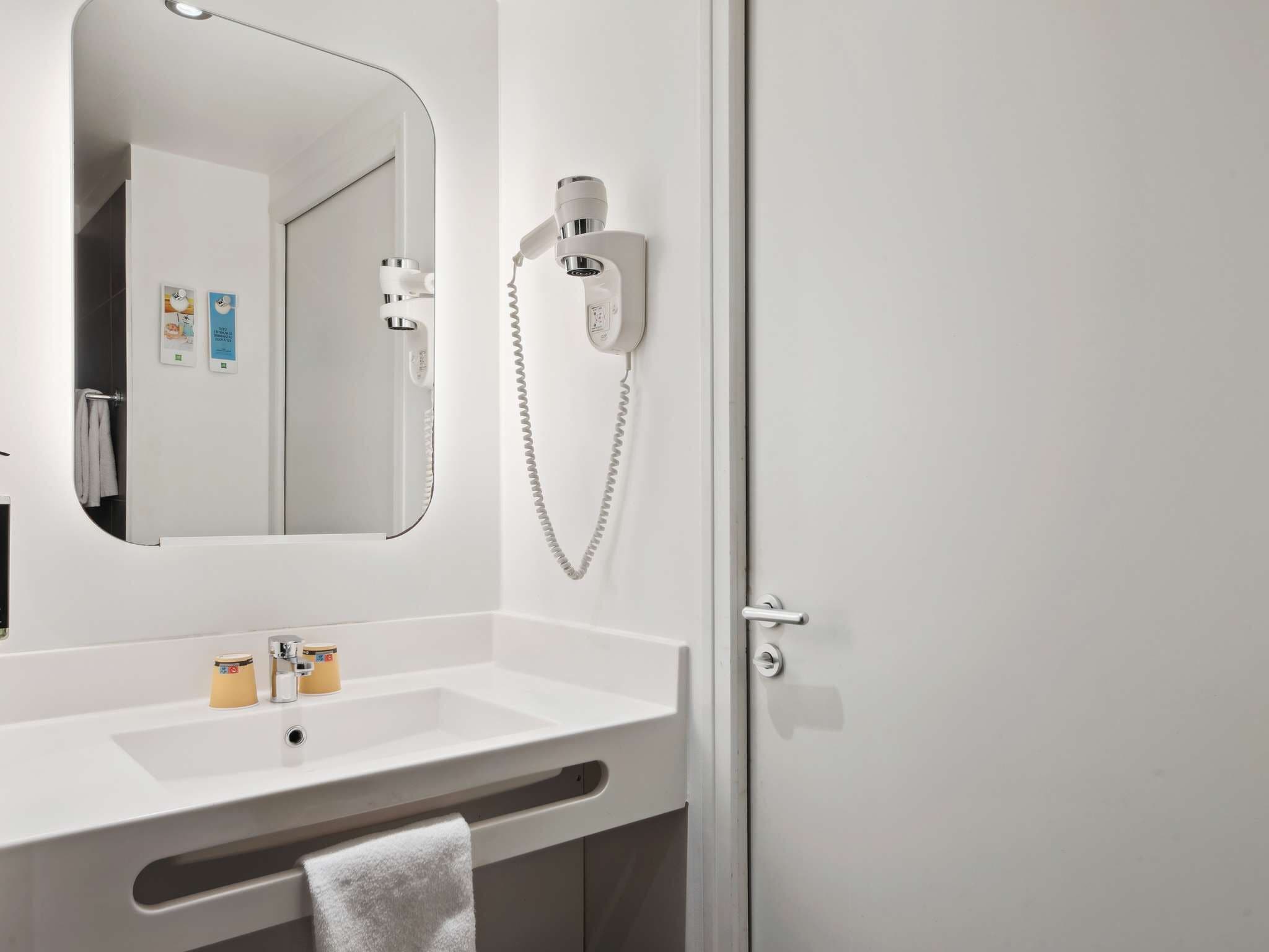 A bathroom with a white sink, a mirror, a hairdryer, and a towel rack.
