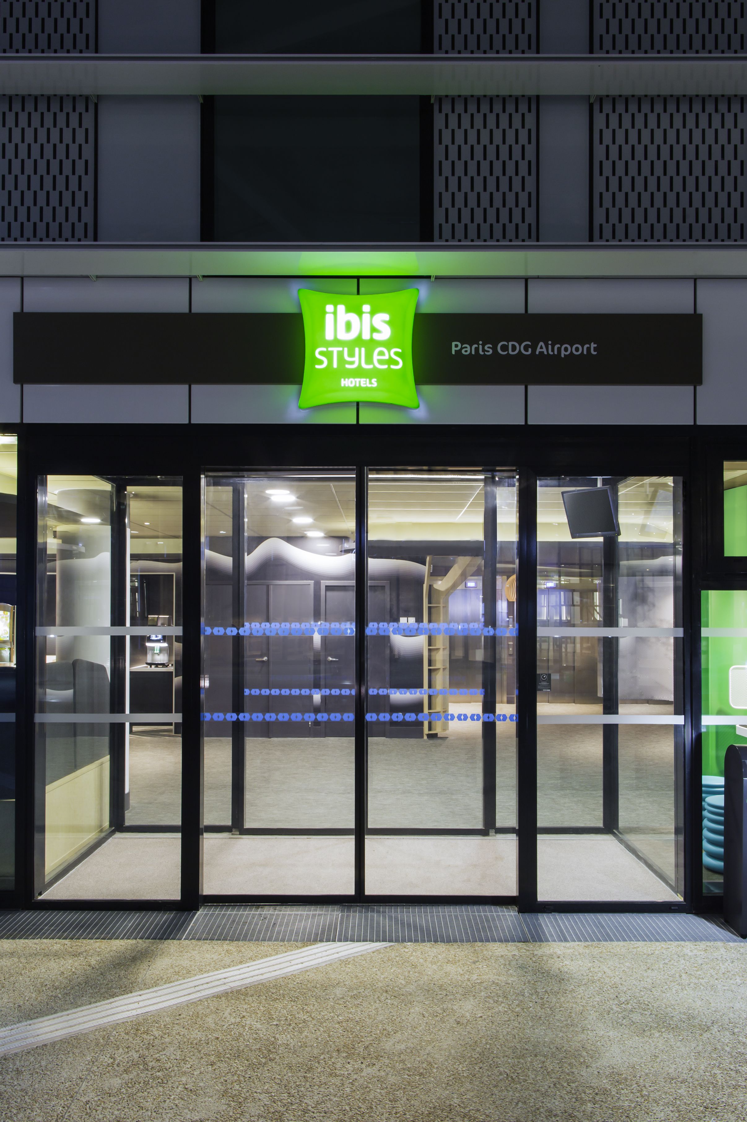 The entrance to ibis Styles Paris CDG Airport hotel with a glass door and a green sign.