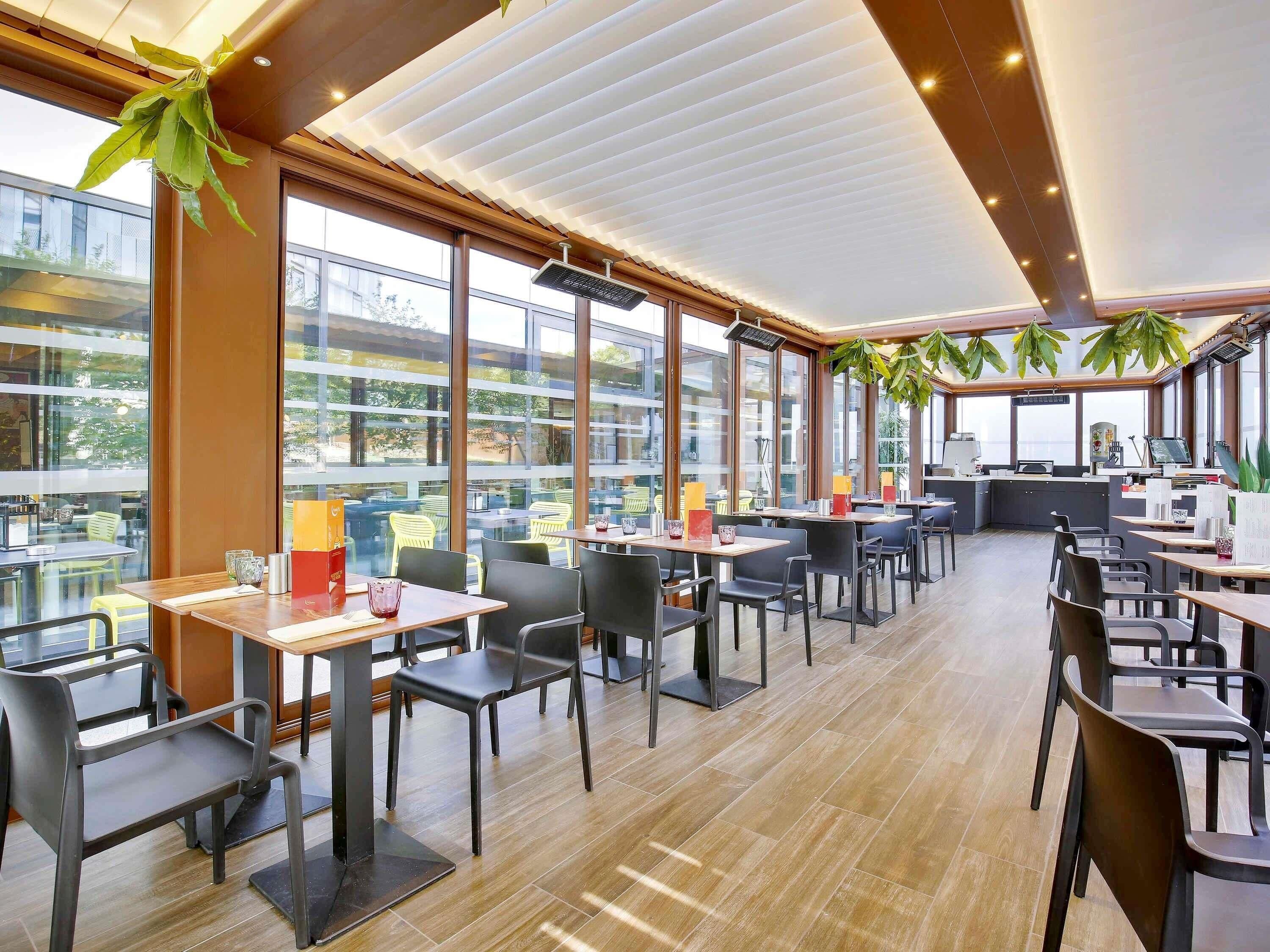 A modern restaurant with large windows, wooden flooring, and black chairs.