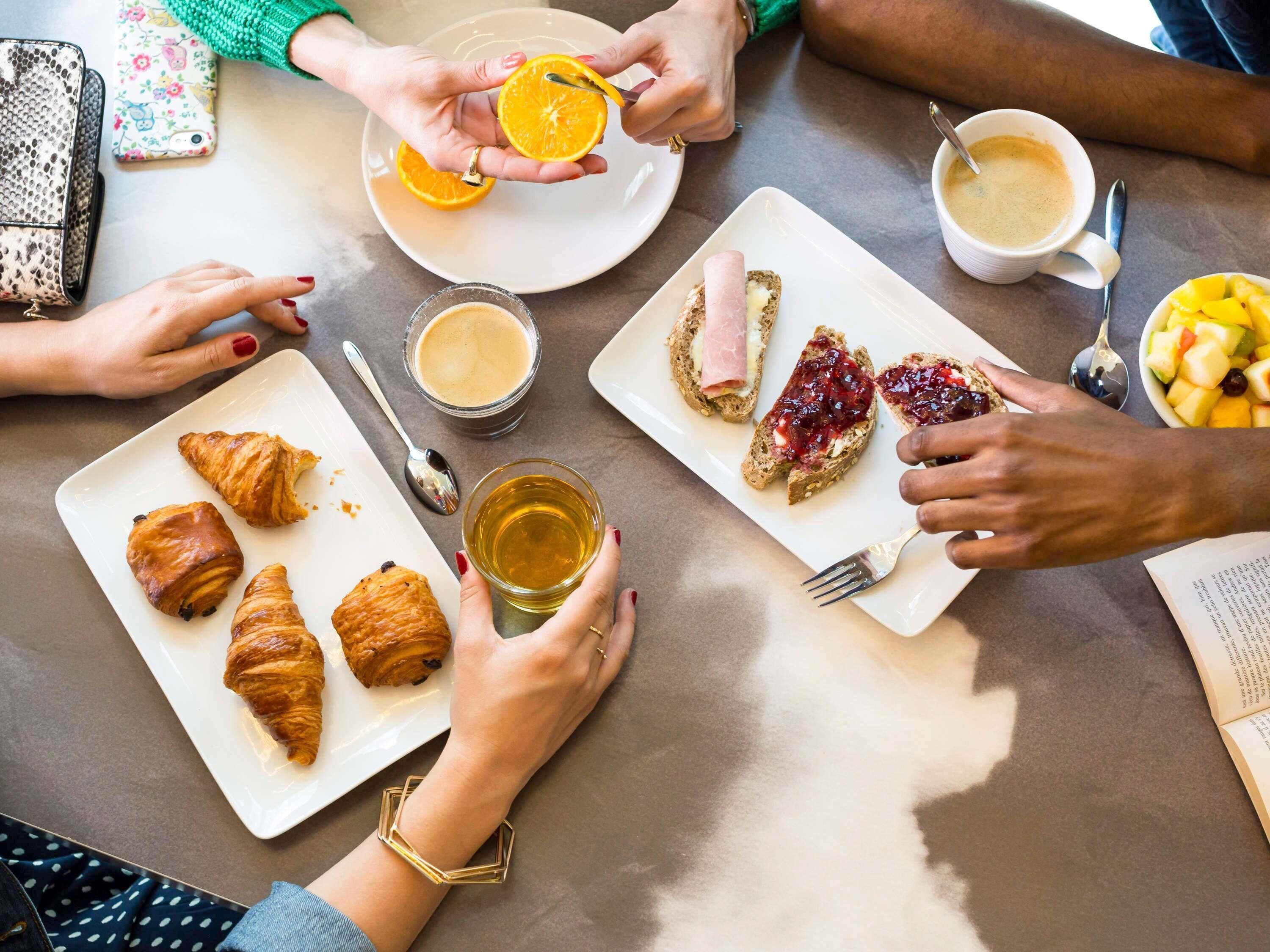 A group of people sharing a meal with croissants, fruit, and coffee at a table.