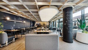 A modern restaurant with a wooden ceiling, black and white decor, and a large black pillar with writing. - Ibis Styles Paris Charles de Gaulle Airport (Tremblay-en-France)