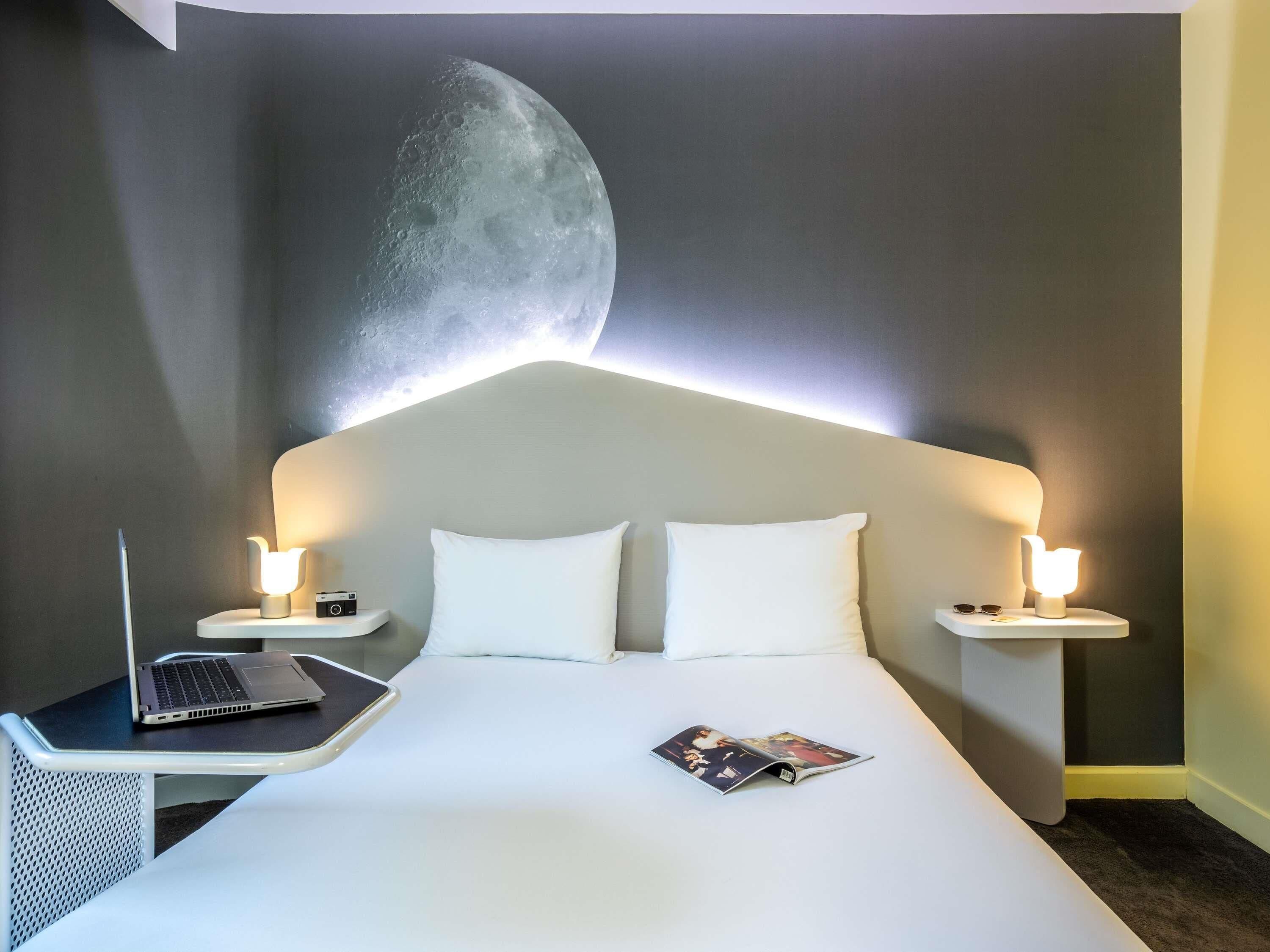 A hotel room with a bed, two bedside tables, a laptop, and a magazine on the bed.