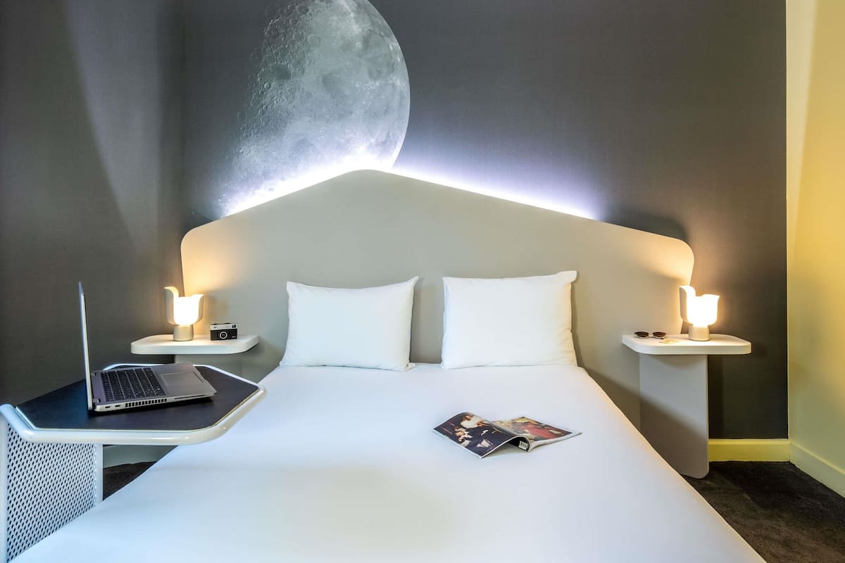 A hotel room with a bed, two bedside tables, a laptop, and a magazine on the bed.