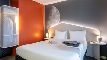 Habitación de hotel moderna con una cama grande, una mesita de noche con lámpara y un televisor montado en la pared.