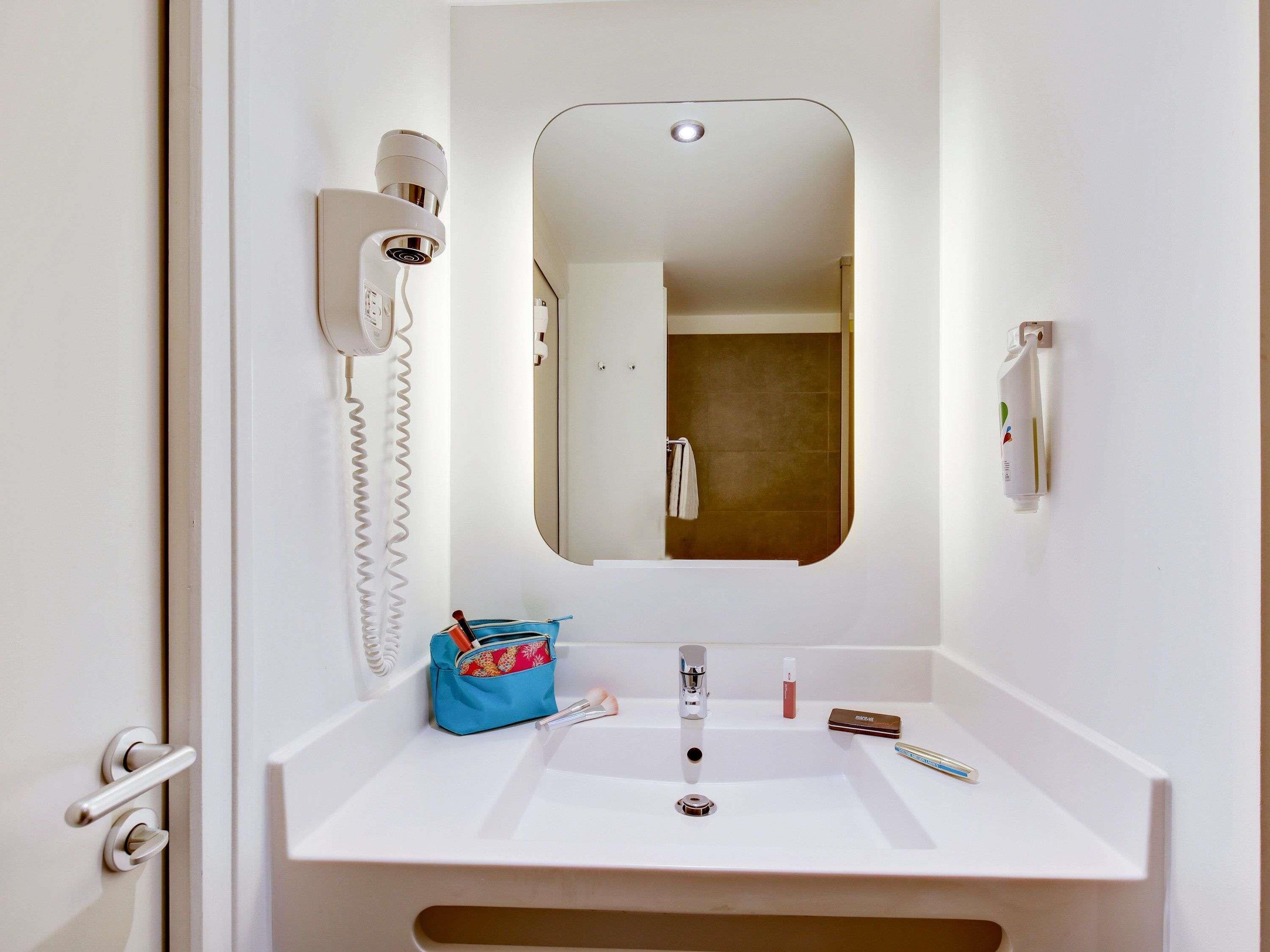 Un baño con lavamanos blanco, un espejo, un secador de pelo y un toallero.