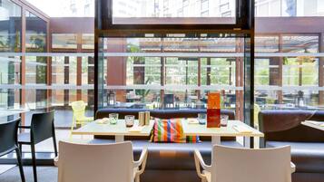 Un comedor moderno con asientos tipo cabina, grandes ventanales que ofrecen vistas de la ciudad, y una mesa con un menú y vasos.