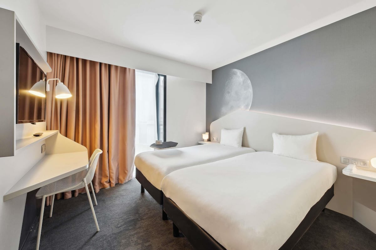 Une chambre d’hôtel équipée d’un bureau, de deux lits, d’un grand miroir et d’une fresque murale.