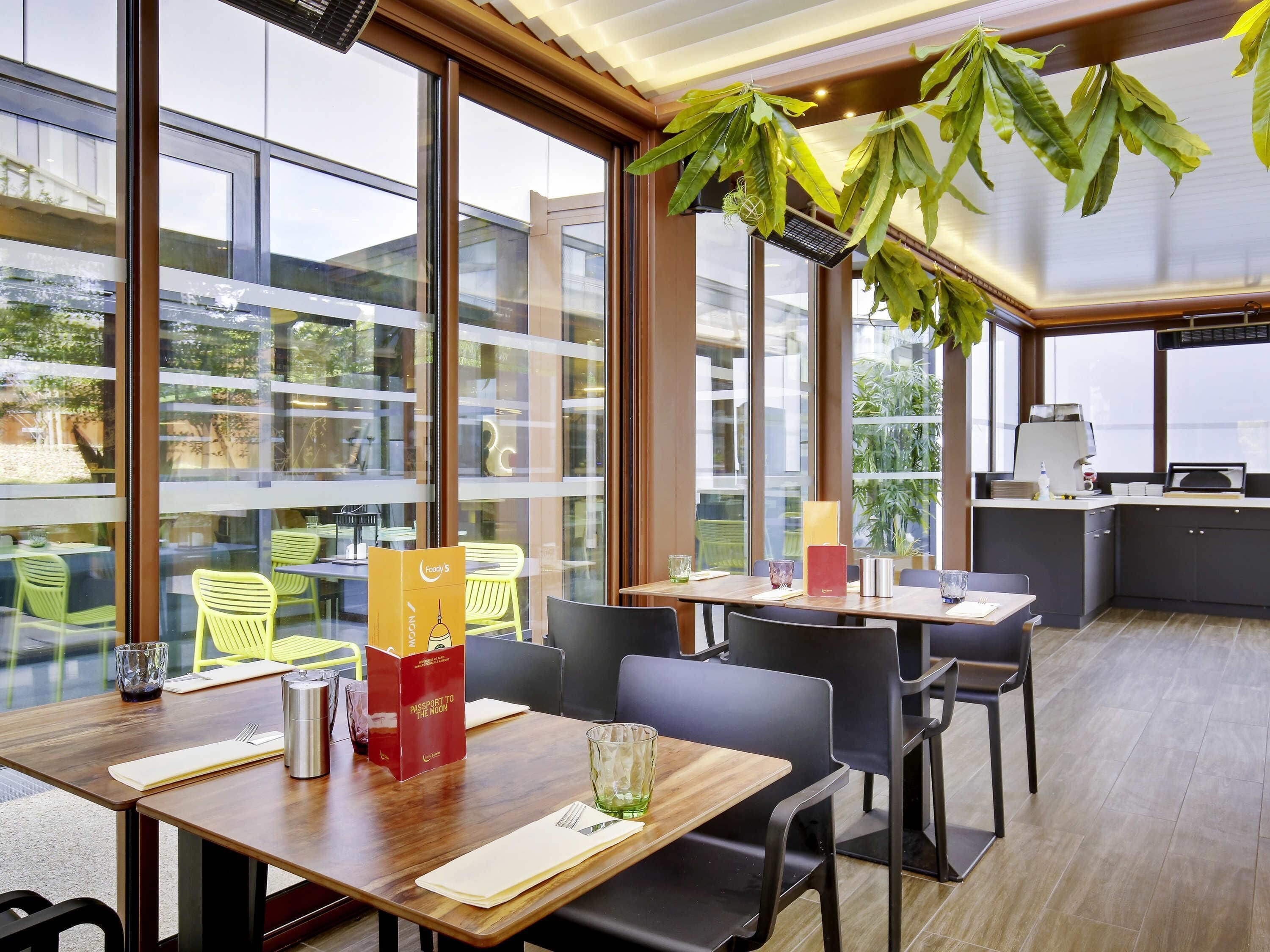 Un restaurante moderno con amplios ventanales, mesas y sillas de madera.