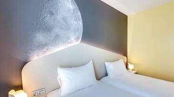 Una camera d'albergo con un letto, due cuscini, un comodino con una lampada e un affresco lunare al muro.