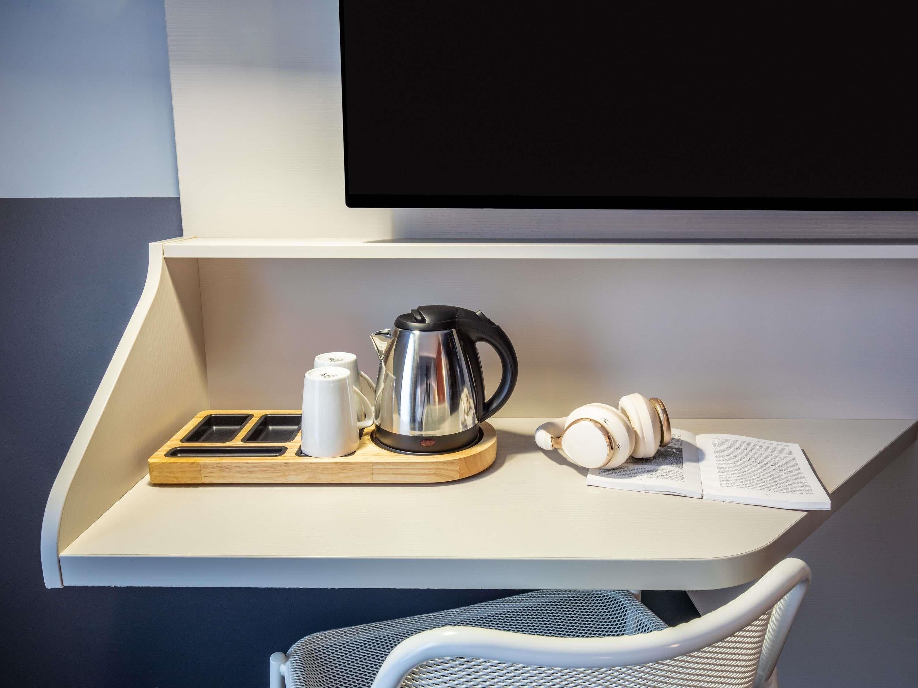 Ein modernes Zimmer mit Schreibtisch, Wasserkocher, Tasse und Kopfhörern.