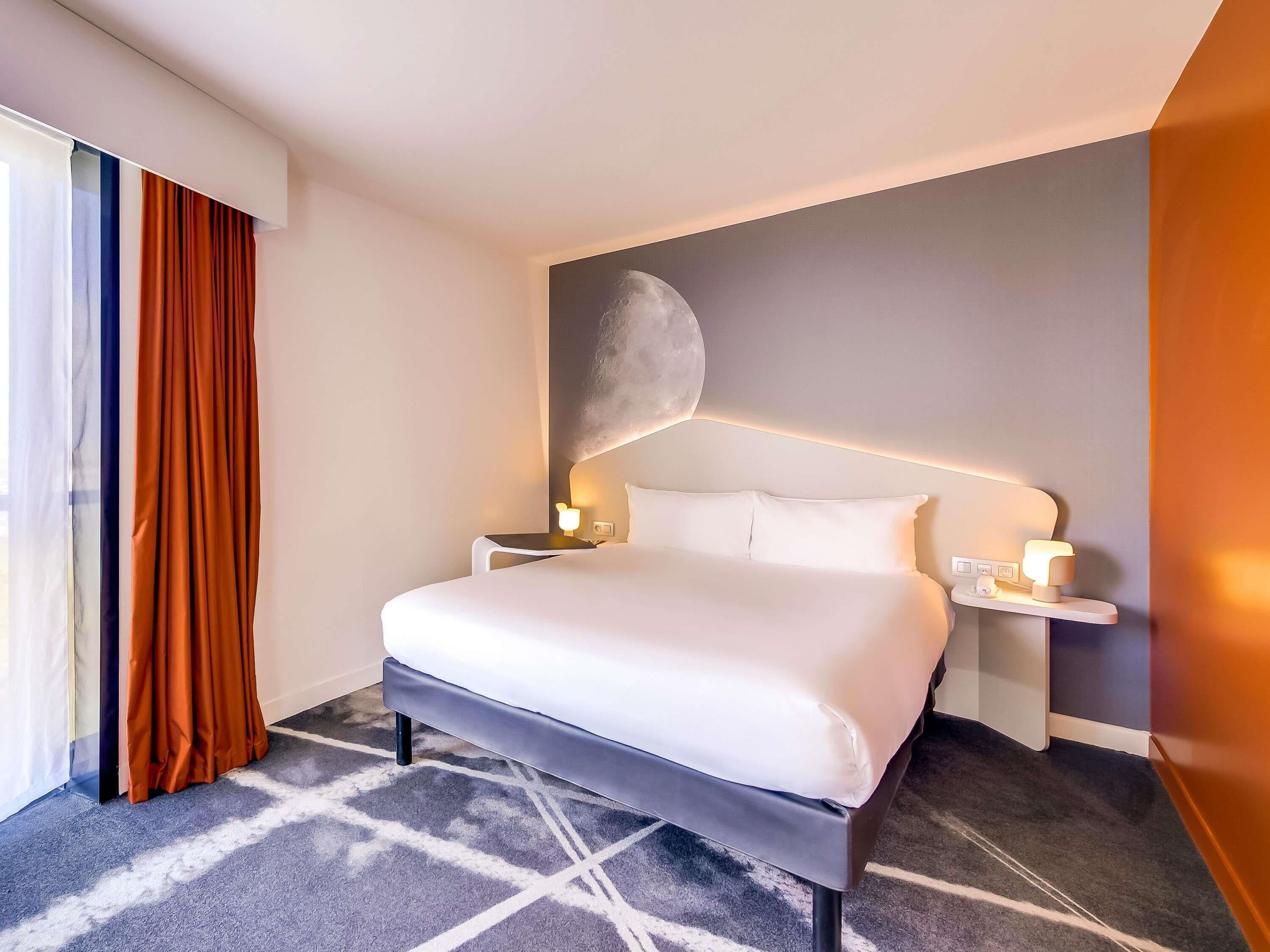 A hotel room with a large bed, a nightstand with a lamp, and a wall-mounted moon decoration.