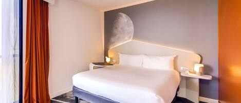 A hotel room with a large bed, a nightstand with a lamp, and a wall-mounted moon decoration.
