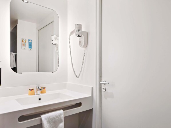 Un baño con un lavabo blanco, un espejo, un secador de pelo y un perchero para toallas.