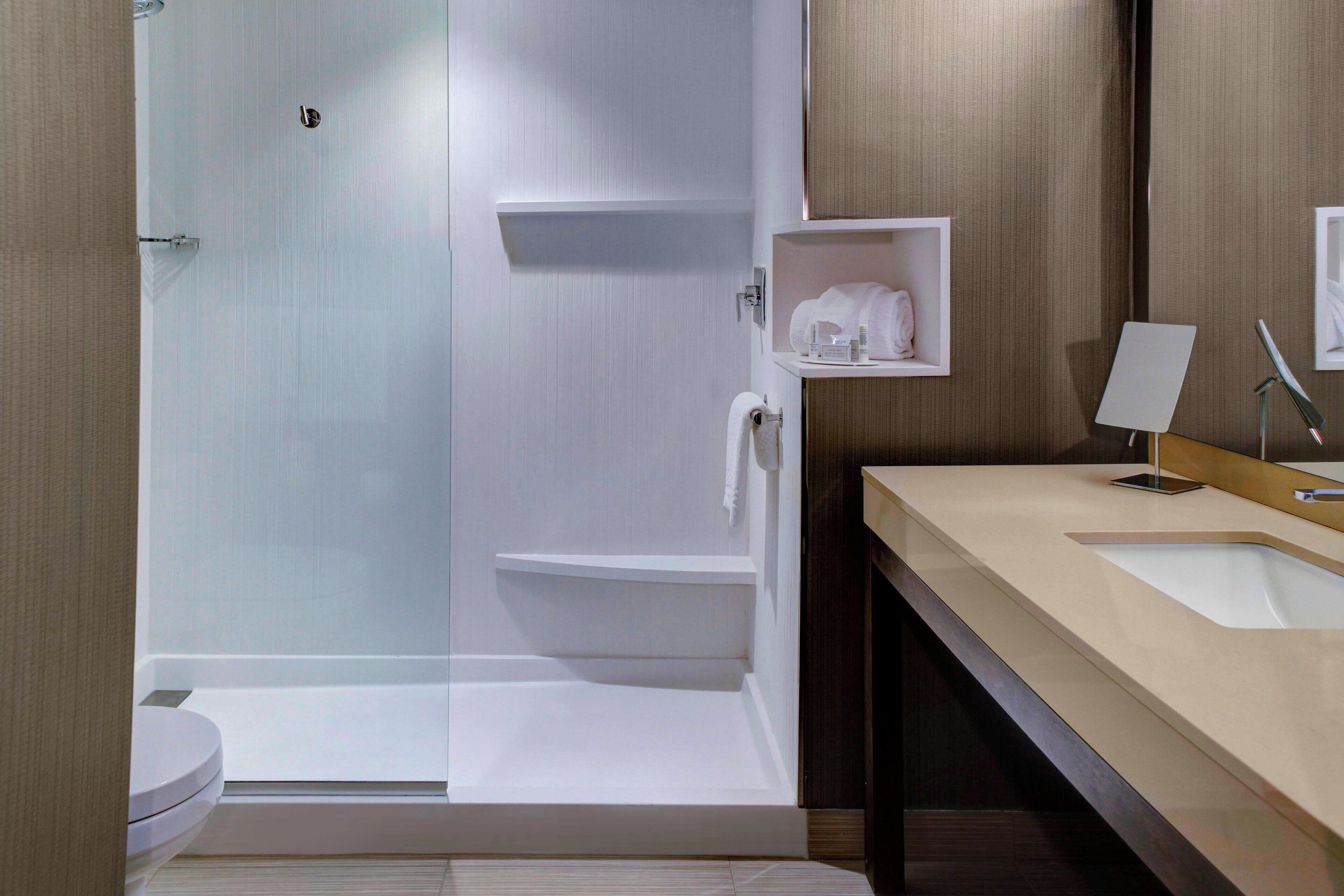 Une salle de bain moderne avec une douche à parois de verre, des toilettes blanches et un meuble-lavabo beige avec un miroir.