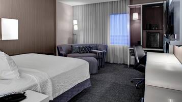 A hotel room with a bed, a sofa, a desk, a chair, a TV, and a minibar.