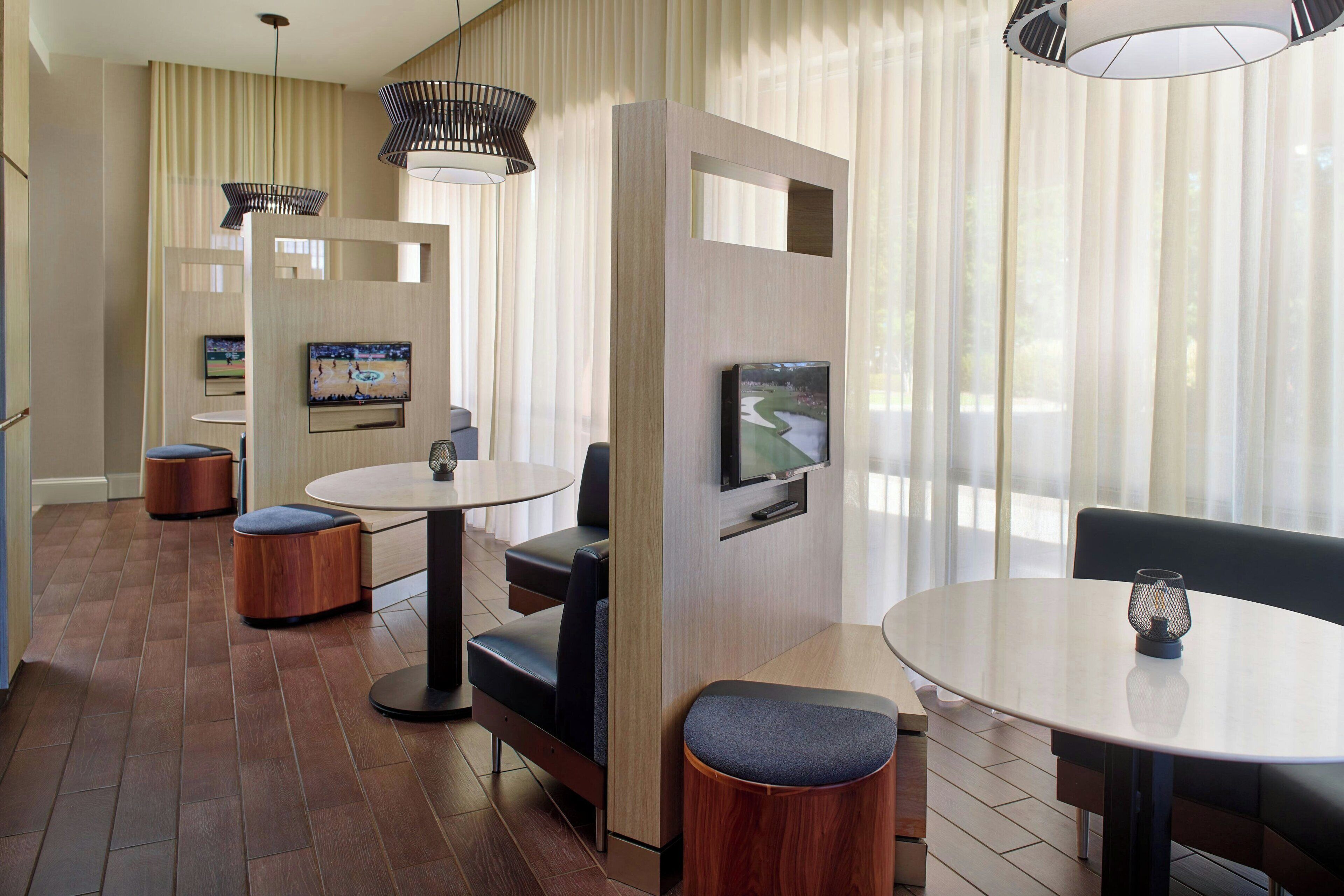 A modern hotel room with a TV, seating area, and large windows.