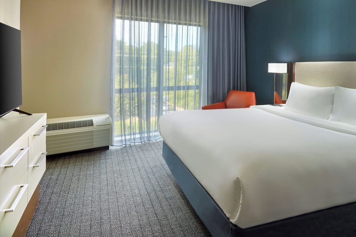 A hotel room with a large bed, a desk with a flat-screen TV, a chair, and a window with curtains.