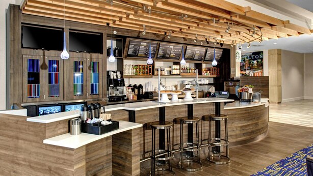 A modern bar area with a wooden ceiling, bar stools, and a counter with a menu board. - Courtyard Carrollton (Carrollton)