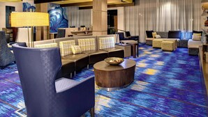 A modern hotel lobby with a blue and yellow carpet, a large abstract painting, and a seating area with sofas and armchairs. - Courtyard Carrollton (Carrollton)