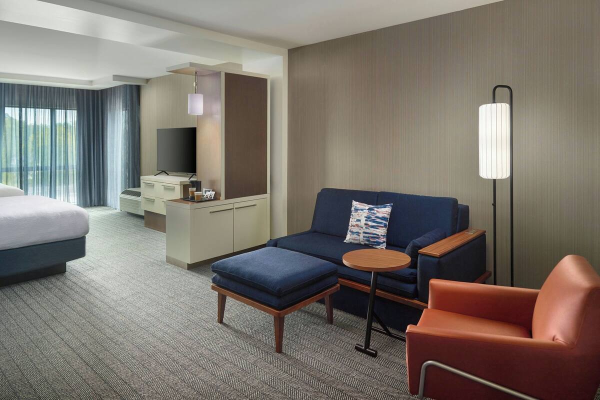 A hotel room with a bed, a sofa, a chair, a desk, and a TV.