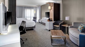 A modern hotel room with a bed, desk, chair, sofa, and TV. - Courtyard Carrollton (Carrollton)