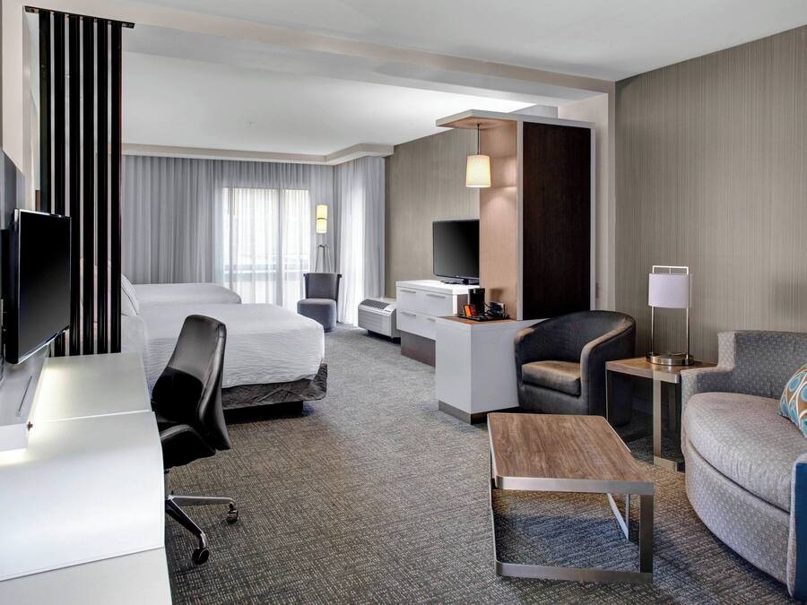 A modern hotel room with a bed, desk, chair, sofa, and TV.