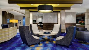 A lobby with a check-in counter, seating area with a round table, and a large wall-mounted TV. - Courtyard Carrollton (Carrollton)