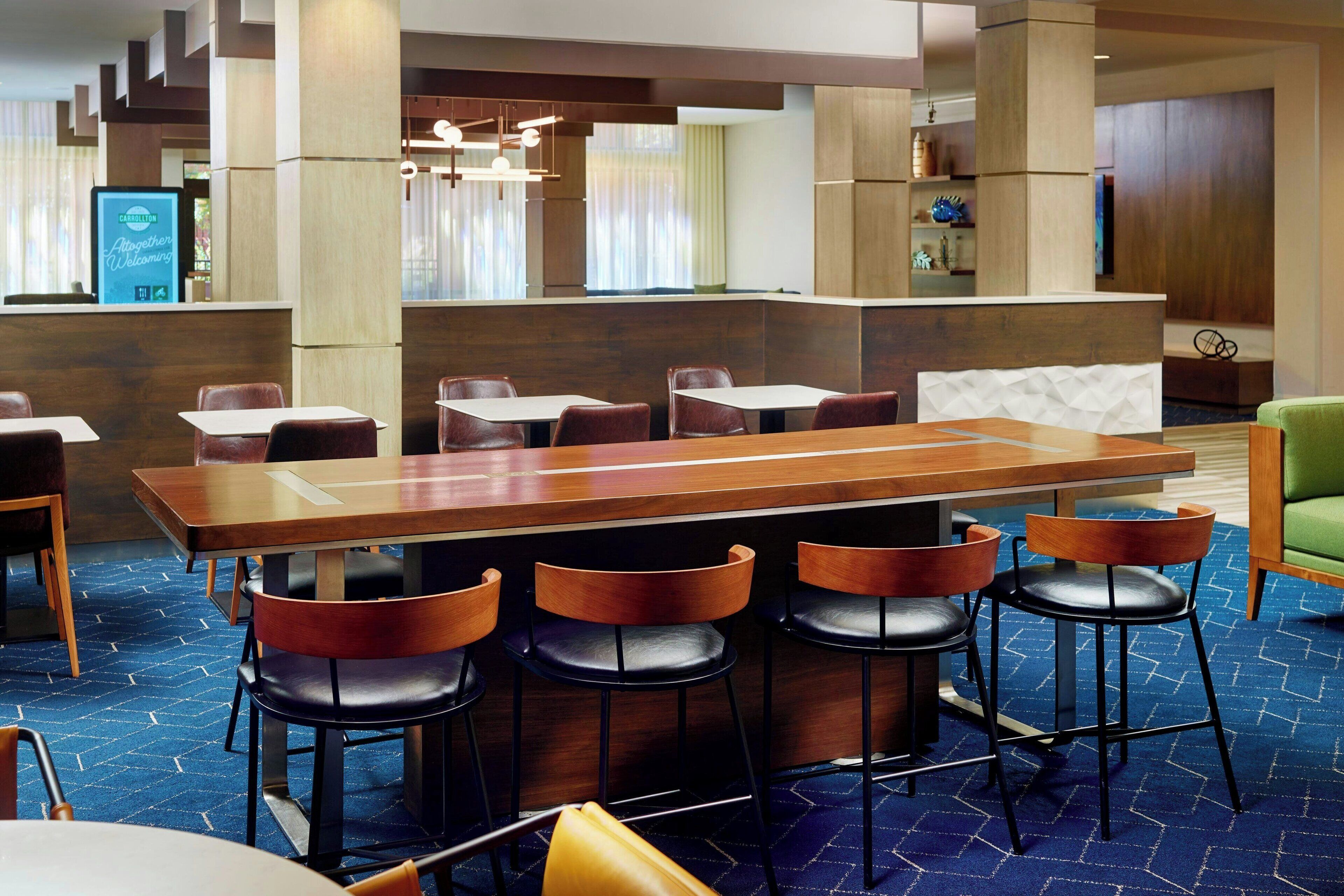 A modern hotel lobby with a central bar area, seating arrangements, and a reception desk.