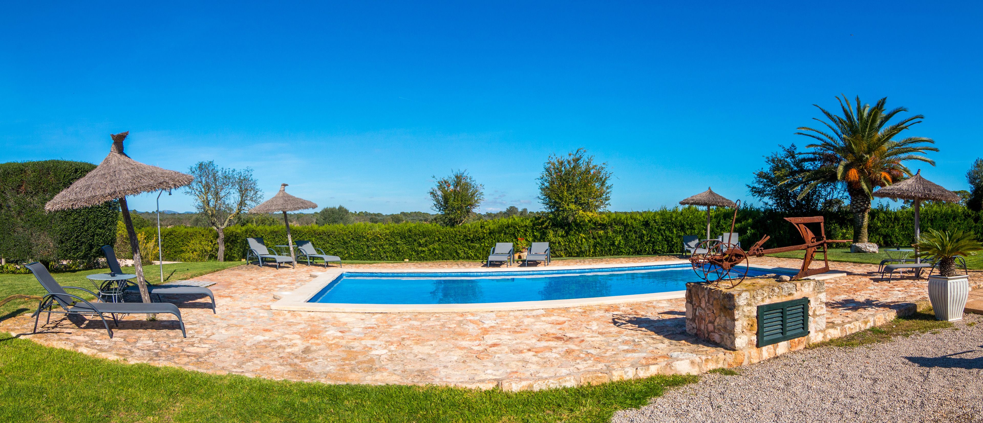 Piscina con sillas de descanso y sombrillas de paja, rodeada de baldosas de piedra y vegetación.
