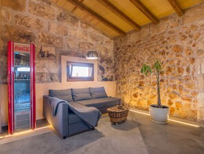 Ein gemütlicher Raum mit einer Steinwand, einem roten Coca-Cola Kühlschrank, einem grauen Sofa, einem kleinen Holztisch und einer Topfpflanze.