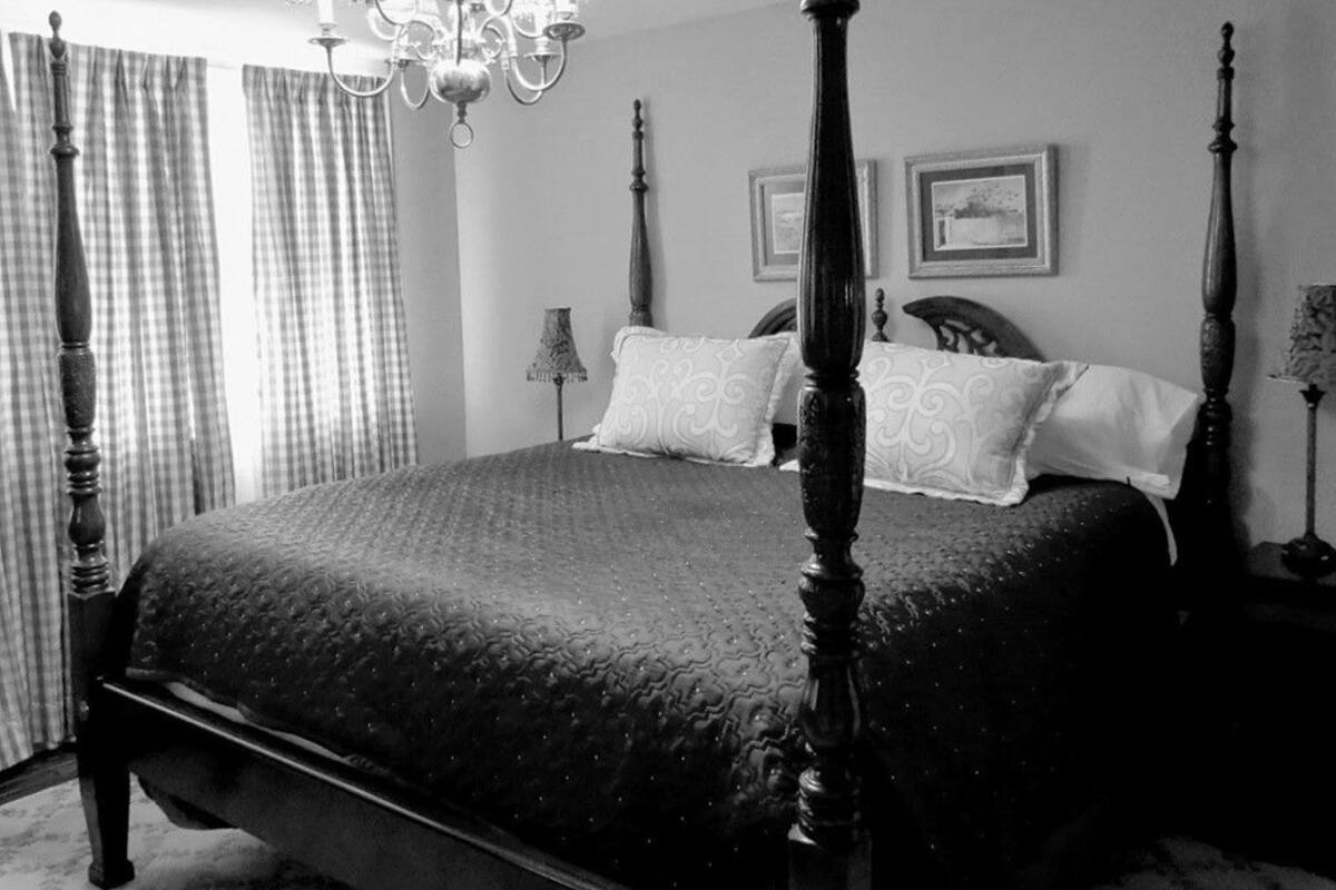 A four-poster bed with a textured bedspread, a chandelier, and two framed pictures on the wall.