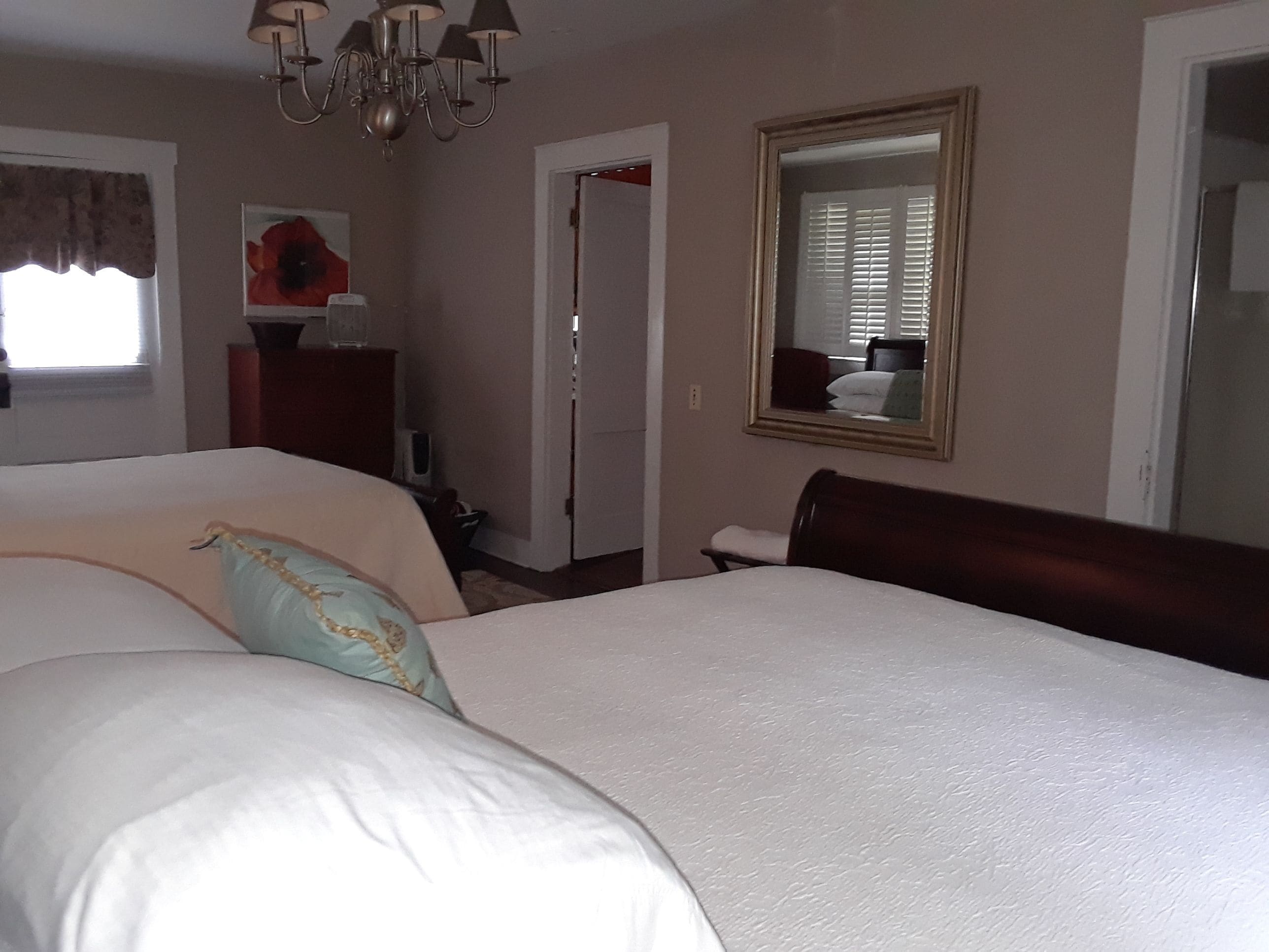 A bedroom with a large bed, a dresser, a mirror, and a chandelier.