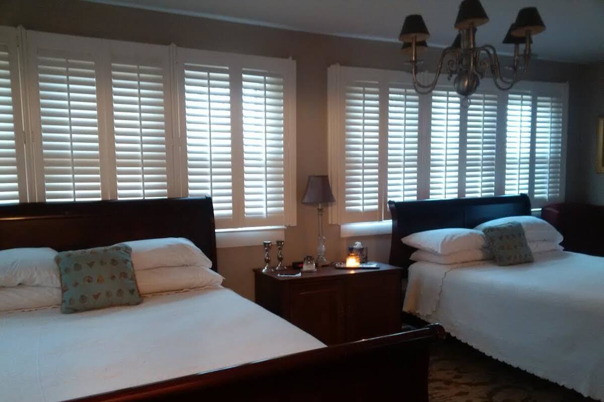 A hotel room with two beds, a nightstand, a lamp, and a chandelier.