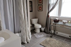 Un baño con inodoro, lavabo, espejo, cortina de ducha y ventana con cortinas.