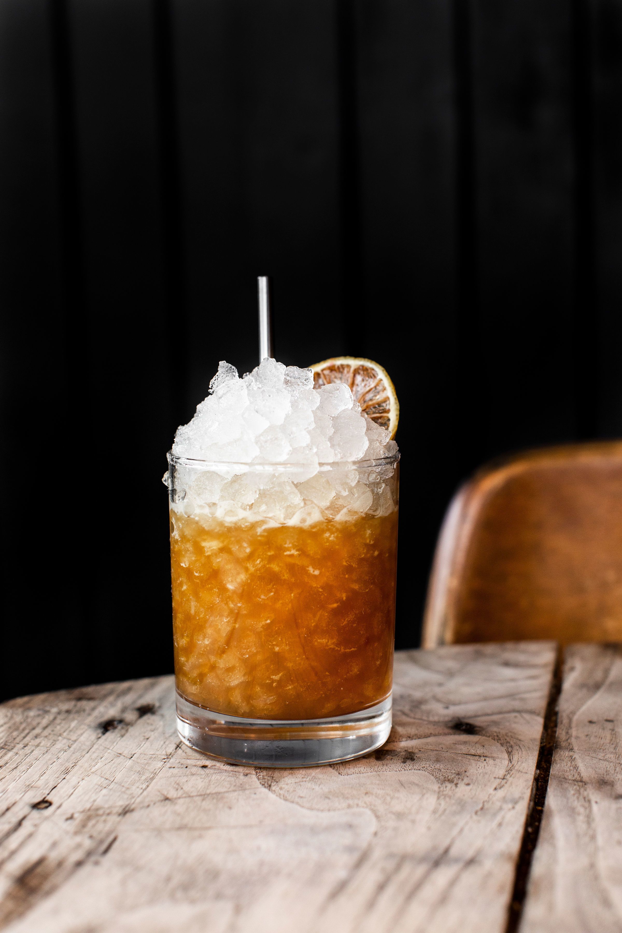 Un verre de thé glacé avec des glaçons et une tranche d’orange, posé sur une table en bois.
