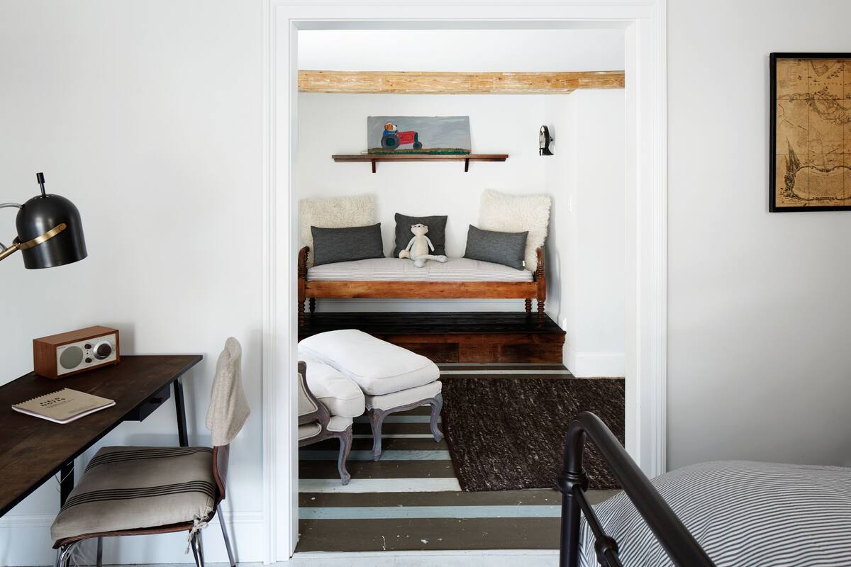 A compact bedroom with a bed, a desk with a chair, a small table with a radio, and a map on the wall.