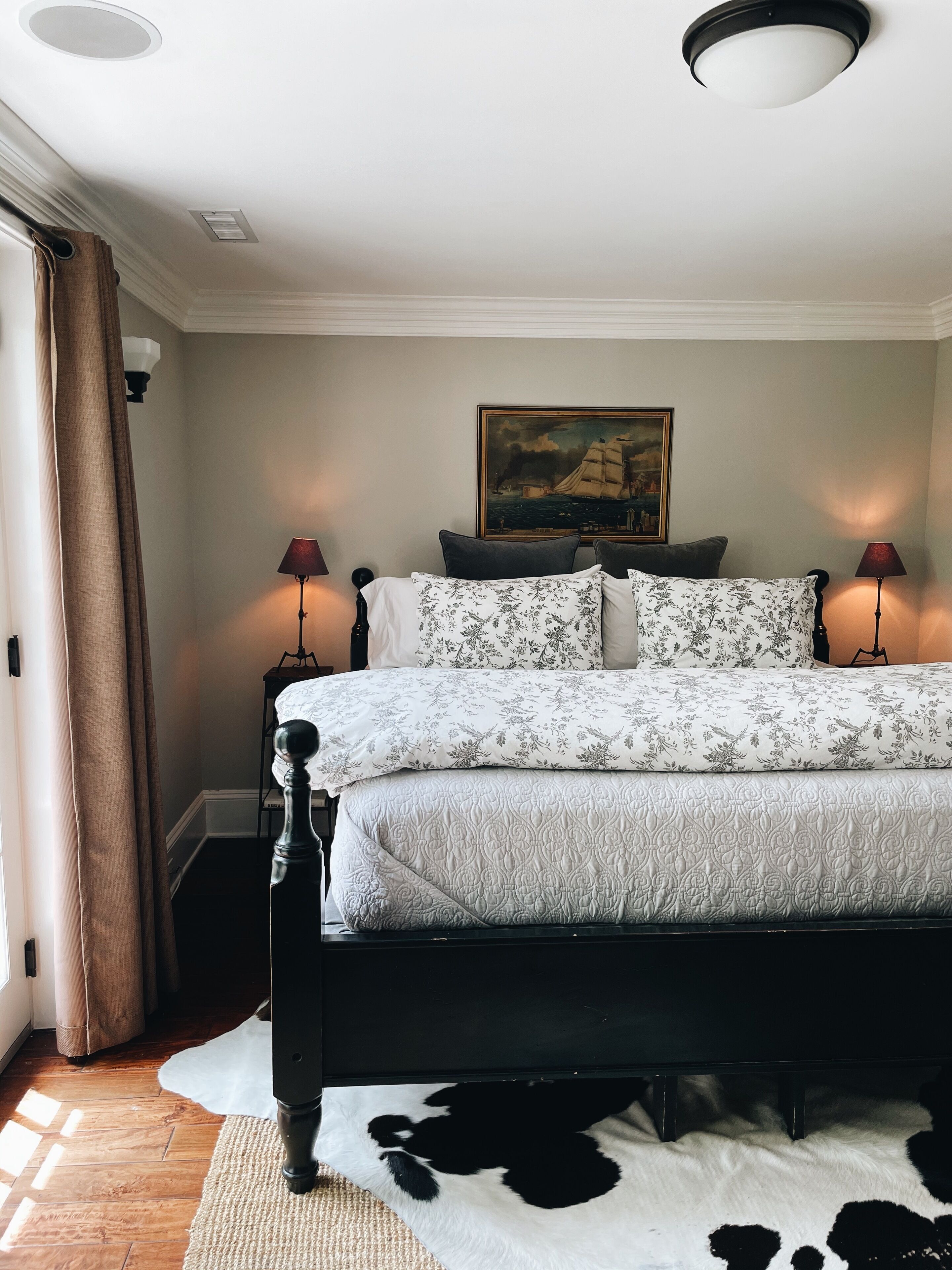 Une chambre à coucher avec un lit, deux lampes de chevet, un tableau au mur et un tapis en peau de vache.