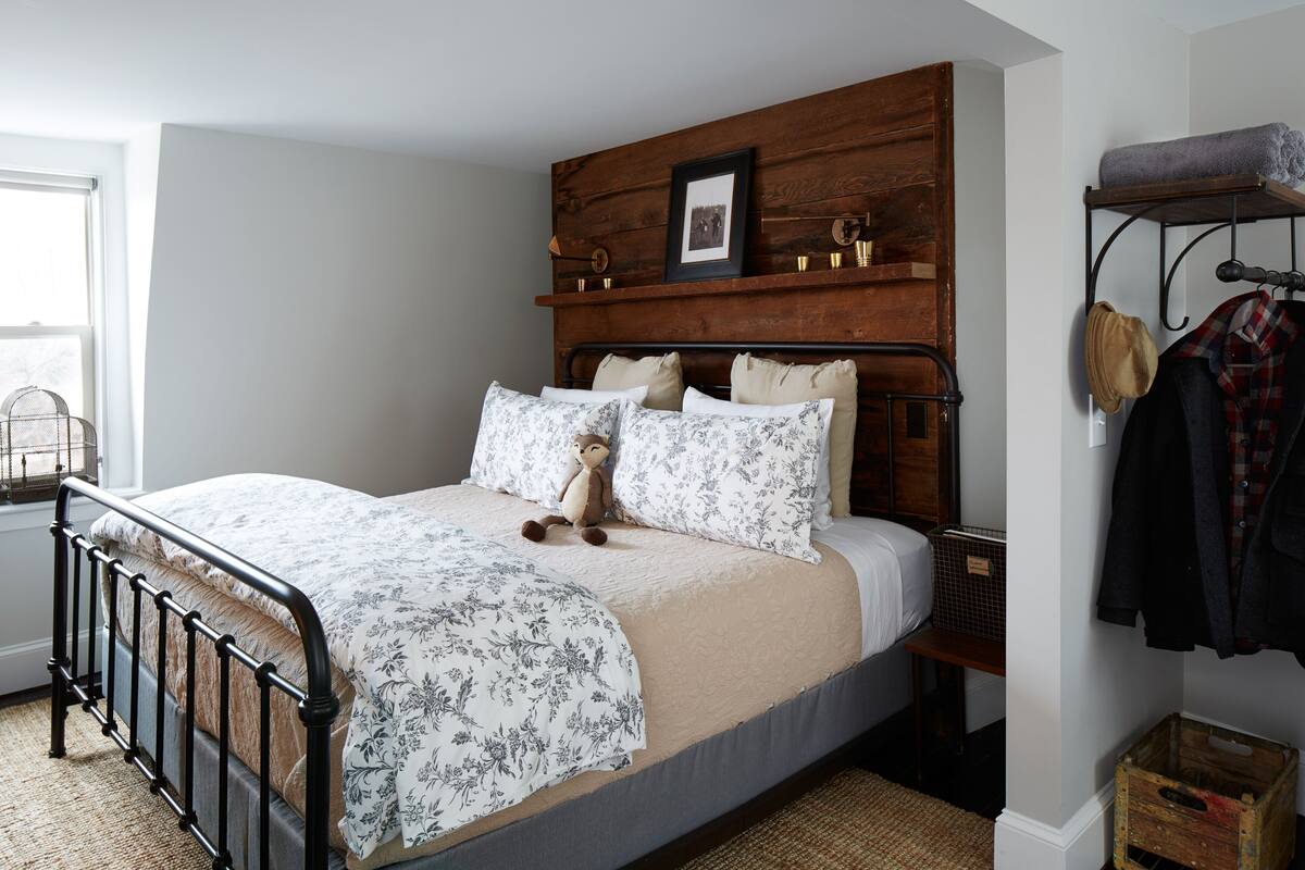 A bedroom with a wooden headboard, a bed with floral bedding, a small bedside table, and a wall-mounted coat rack.