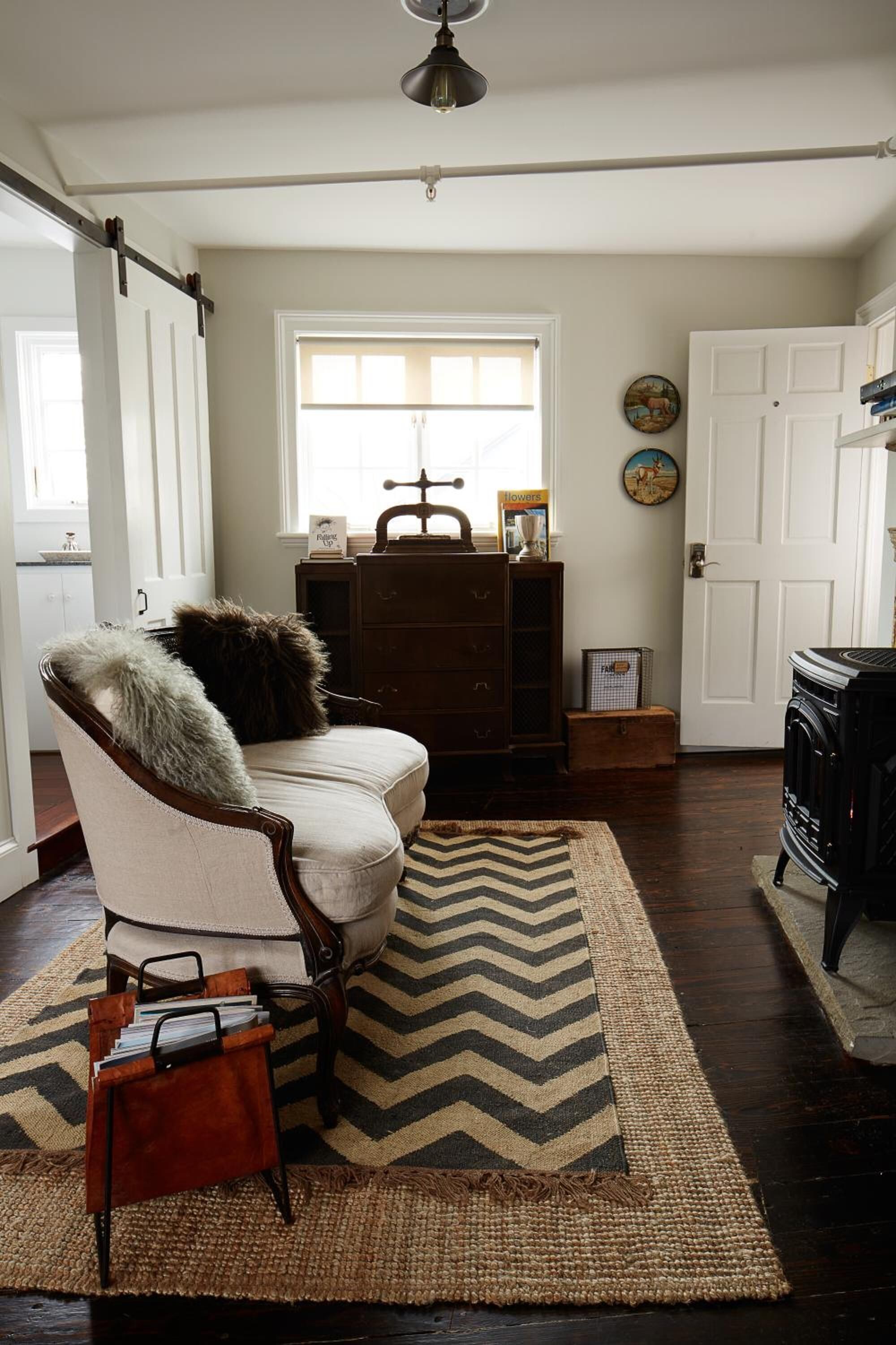 Een gezellige woonkamer met een open haard, een houten dressoir en een fauteuil met een bont plaid.