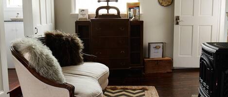Een gezellige woonkamer met een open haard, een houten dressoir en een fauteuil met een bont plaid.