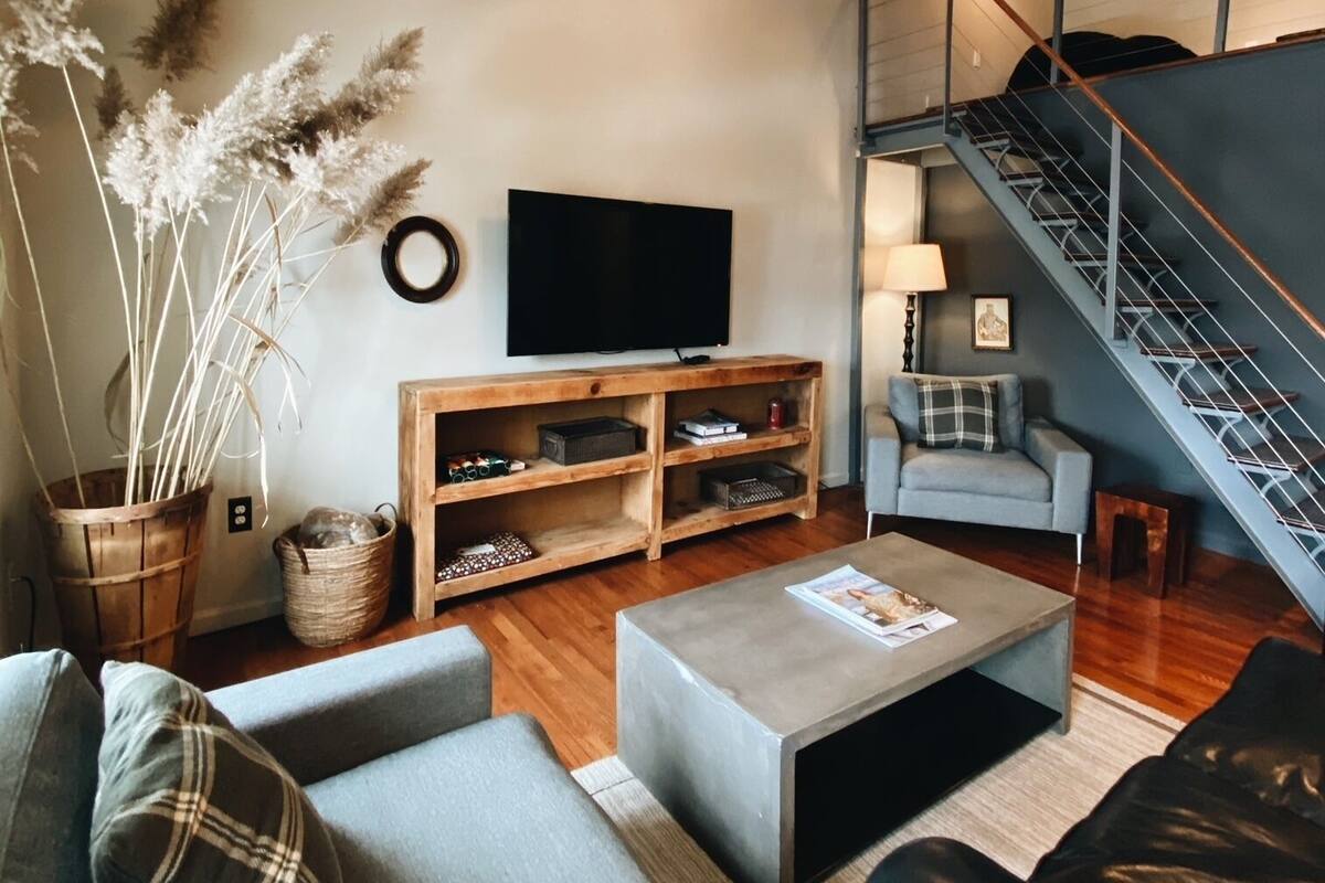 A modern living room with a sofa, coffee table, TV, wooden shelves, and a staircase.